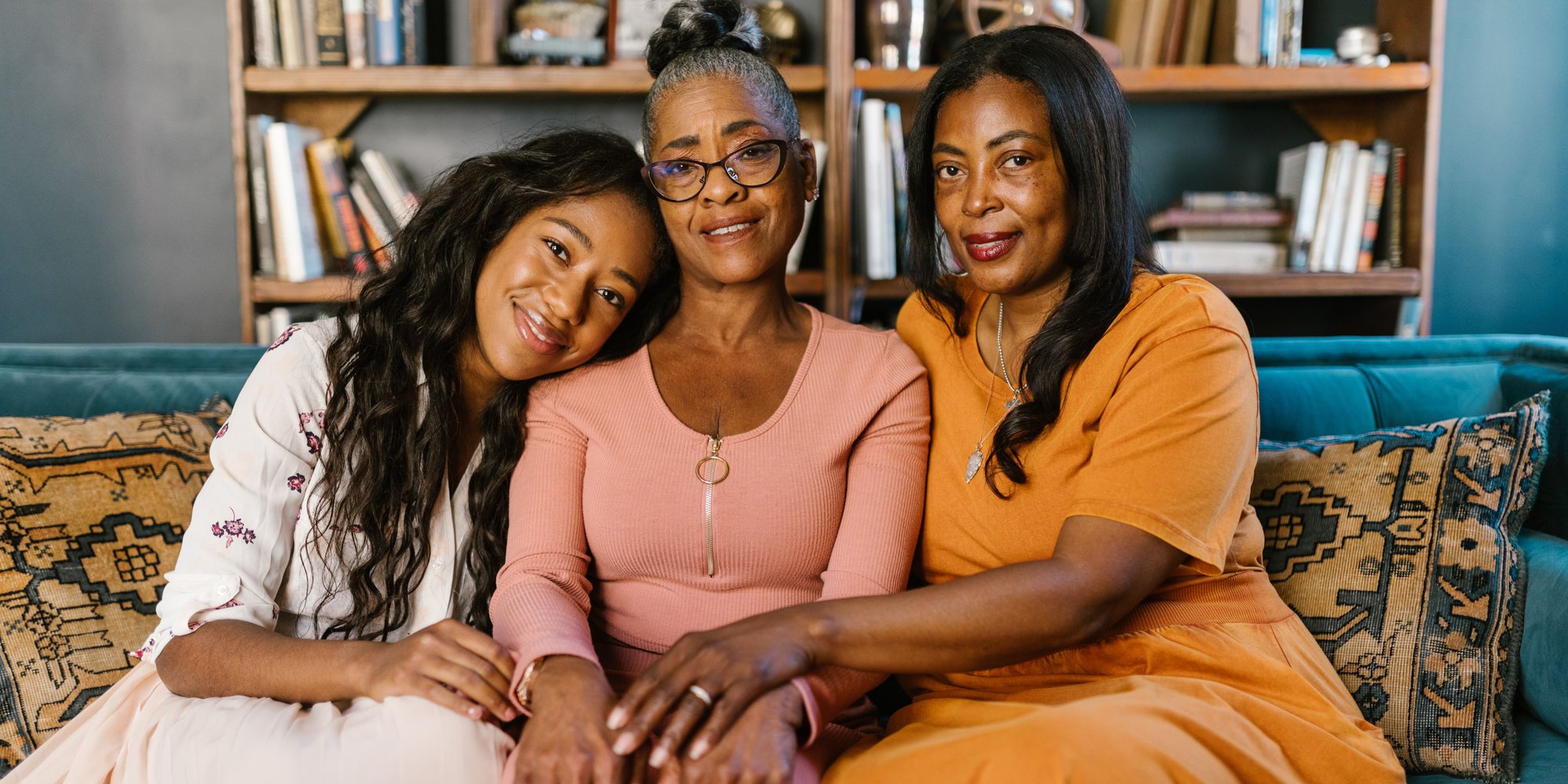 A woman seated between her two adult daughters, their hands resting together in her lap